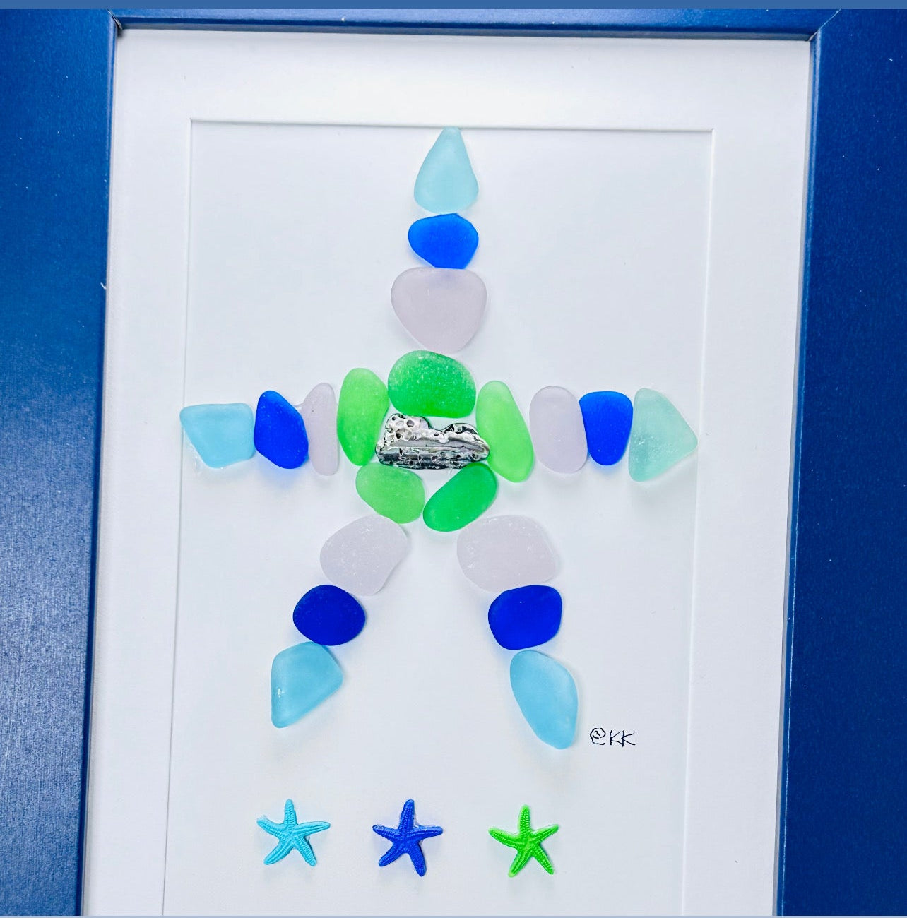 Framed artwork with a starfish made of blue, green, and white glass pieces on a white background.